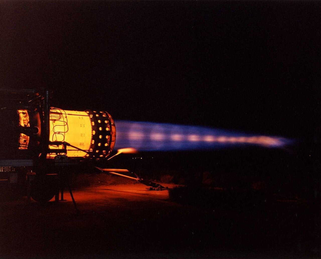 A Pratt and Whitney J58 engine on a static test stand at night in full afterburner, with a blue exhaust plume showing a chain of bright shock diamonds