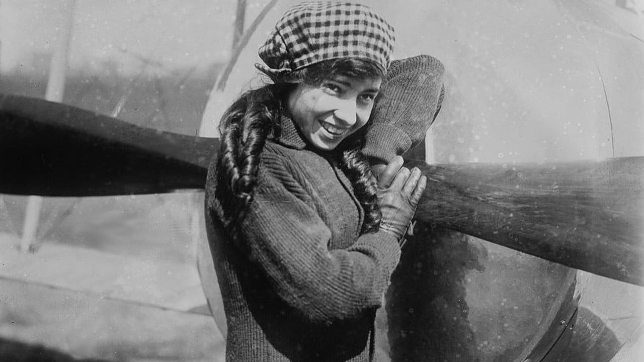 Young aviator Katherine Stinson in a checked cap and knitted sweater smiling as she hugs the propeller of her aircraft