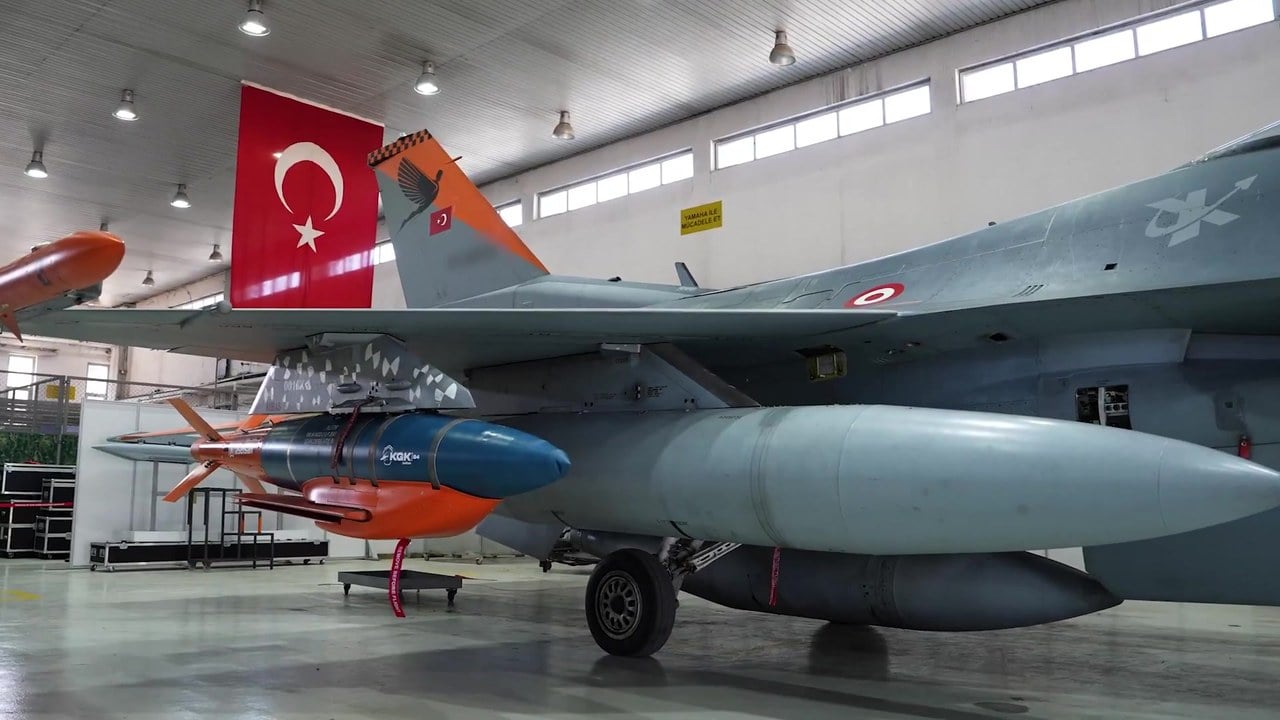 A KGK-84 winged guidance kit mounted under the wing of a Turkish Air Force F-16 inside a hangar with a Turkish flag