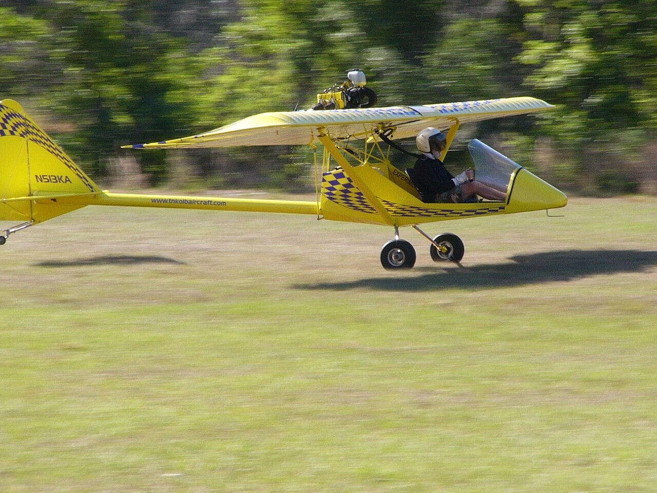 A yellow Kolb Firestar registered N513KA flying low over grass
