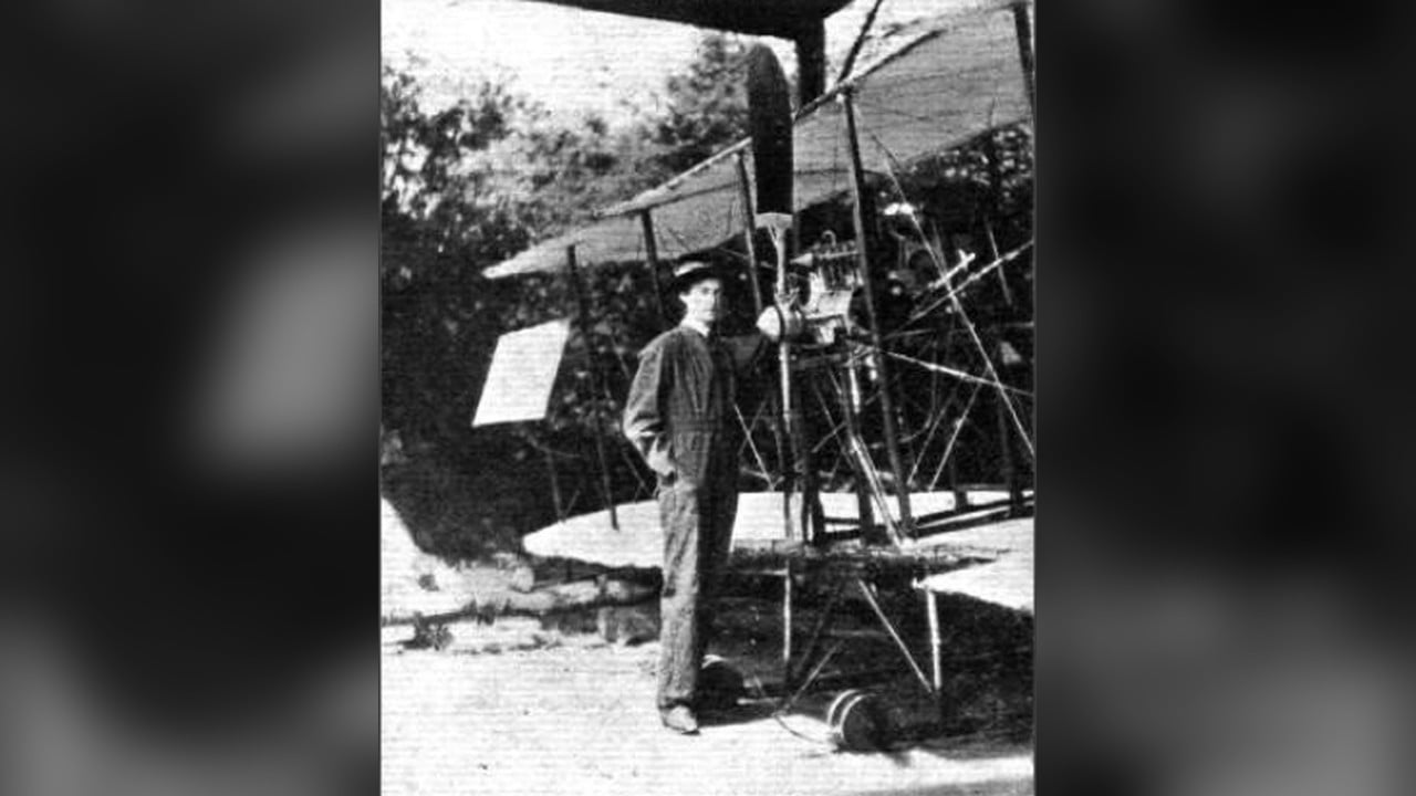 Lilian Bland with the Mayfly, 1910 Lilian Bland in overalls and a hat standing beside the engine of her Mayfly biplane in 1910