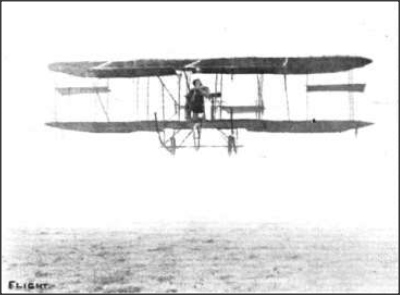 The Mayfly biplane in flight a few feet above a field, with Lilian Bland seated between the wings