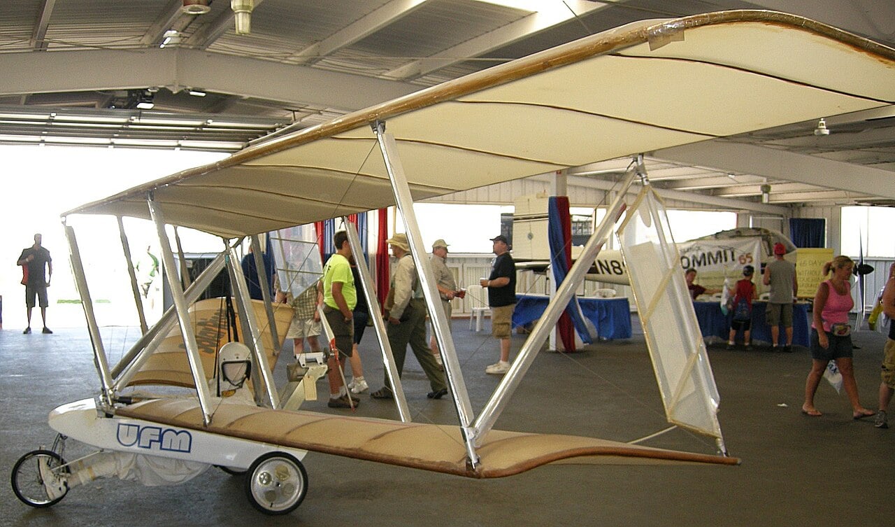 UFM Solar Riser ultralight with solar panels on its upper wing displayed in a hangar at EAA AirVenture Oshkosh