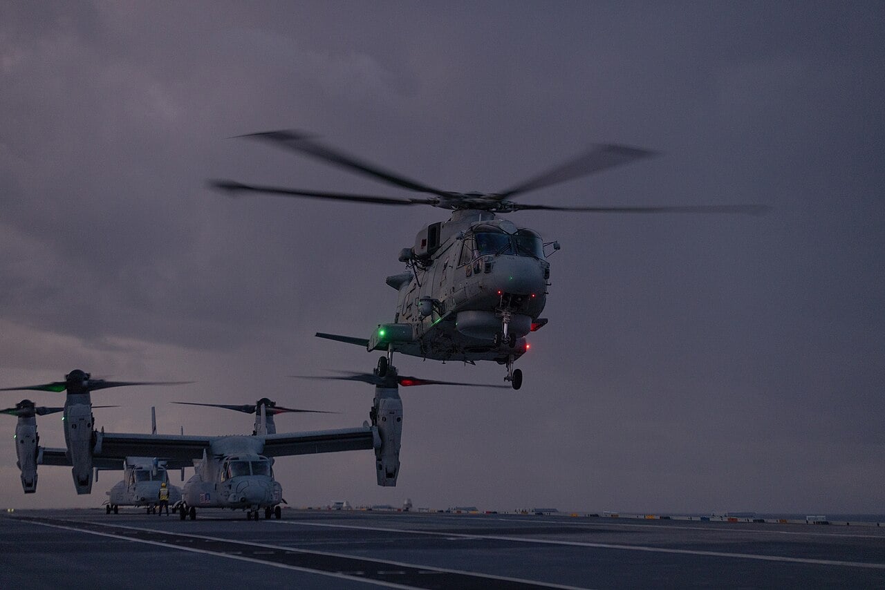 Royal Navy Merlin Mk2 helicopter of 820 Naval Air Squadron landing on HMS Prince of Wales at dusk