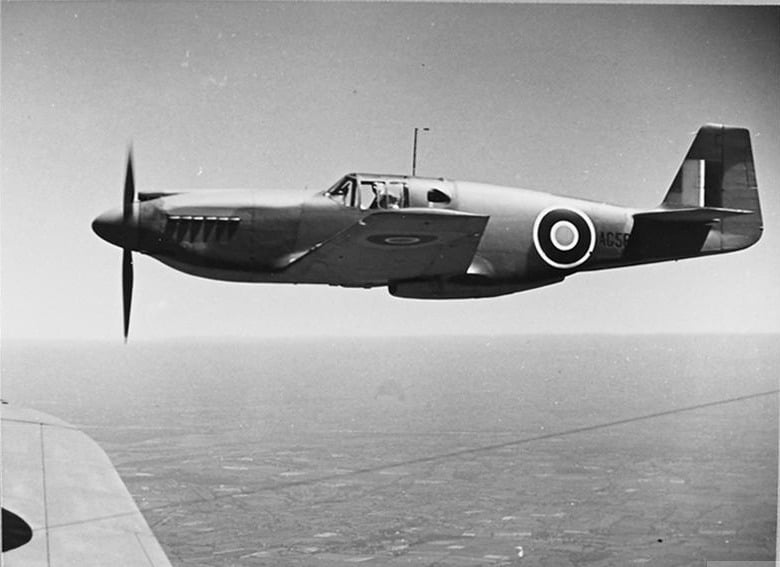 An early Allison-engined North American Mustang Mk I in RAF roundels flying over English farmland, photographed from another aircraft
