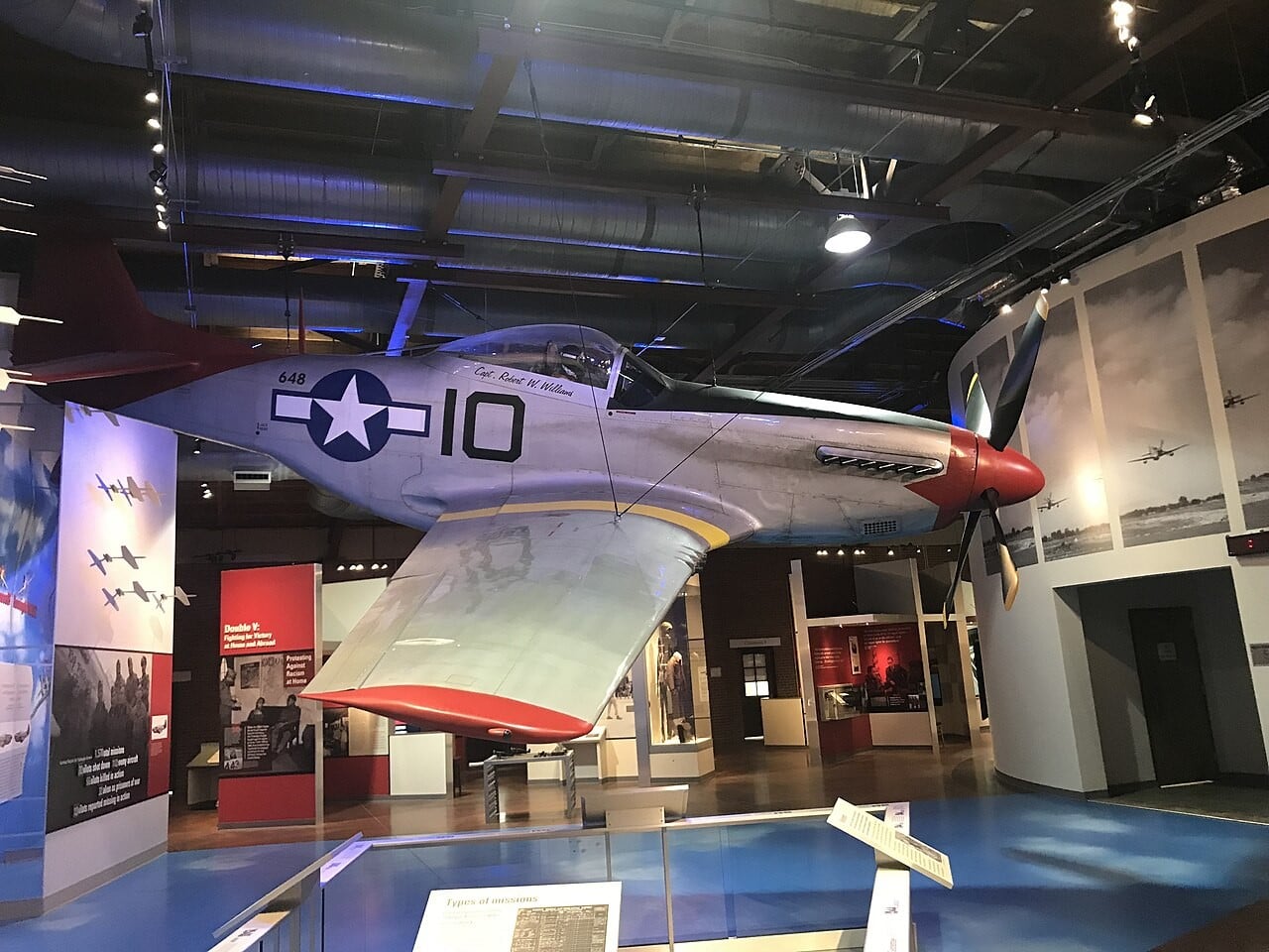 A P-51 Mustang with a red tail and red nose suspended inside Hangar 2 at the Tuskegee Airmen National Historic Site