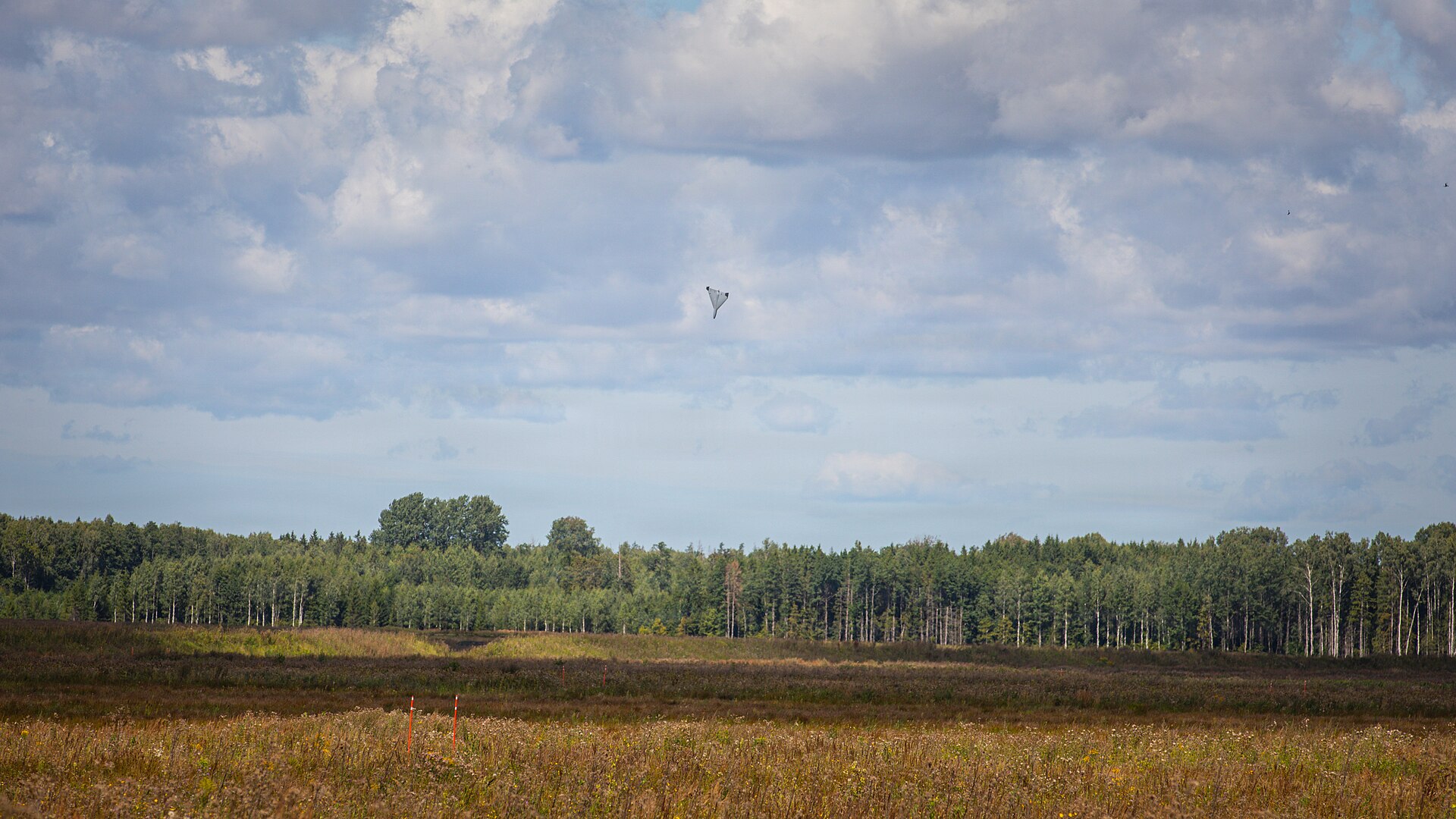 A small drone seen as a dark speck against cloud over a military range