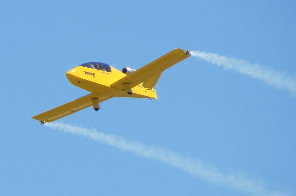 A yellow Sonex SubSonex JSX-1 single-seat homebuilt jet flying with smoke on, EXPERIMENTAL lettering visible on the fuselage