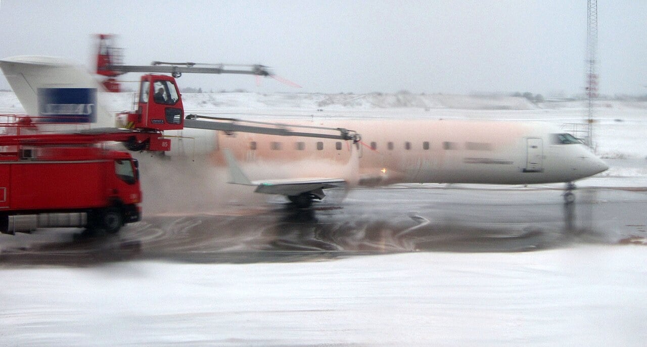 A regional jet being sprayed with orange Type I de-icing fluid from a de-icing truck at Copenhagen Airport in the snow