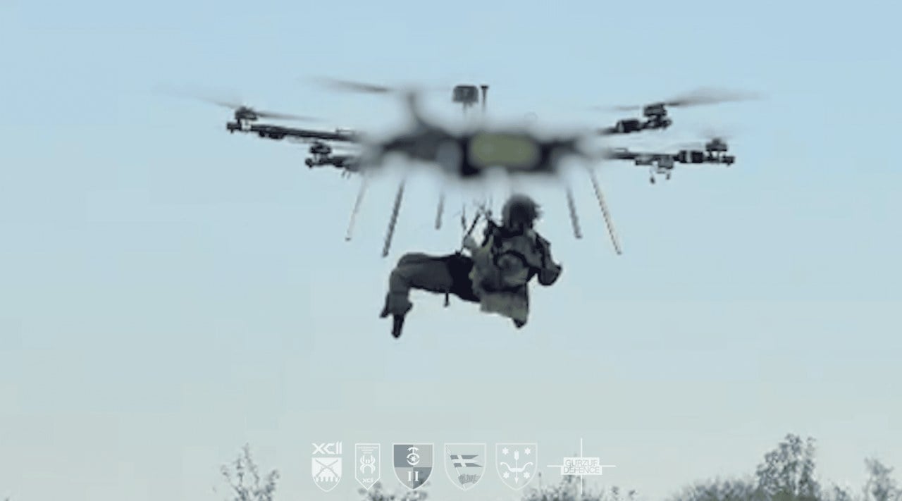 Wounded Ukrainian soldier hanging in a harness beneath a heavy hexacopter drone in flight, still from 92nd Assault Brigade video