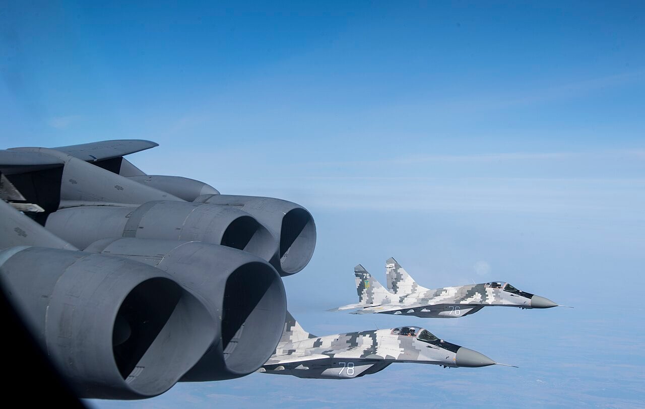 Two Ukrainian Air Force MiG-29s in digital camouflage flying alongside a B-52H