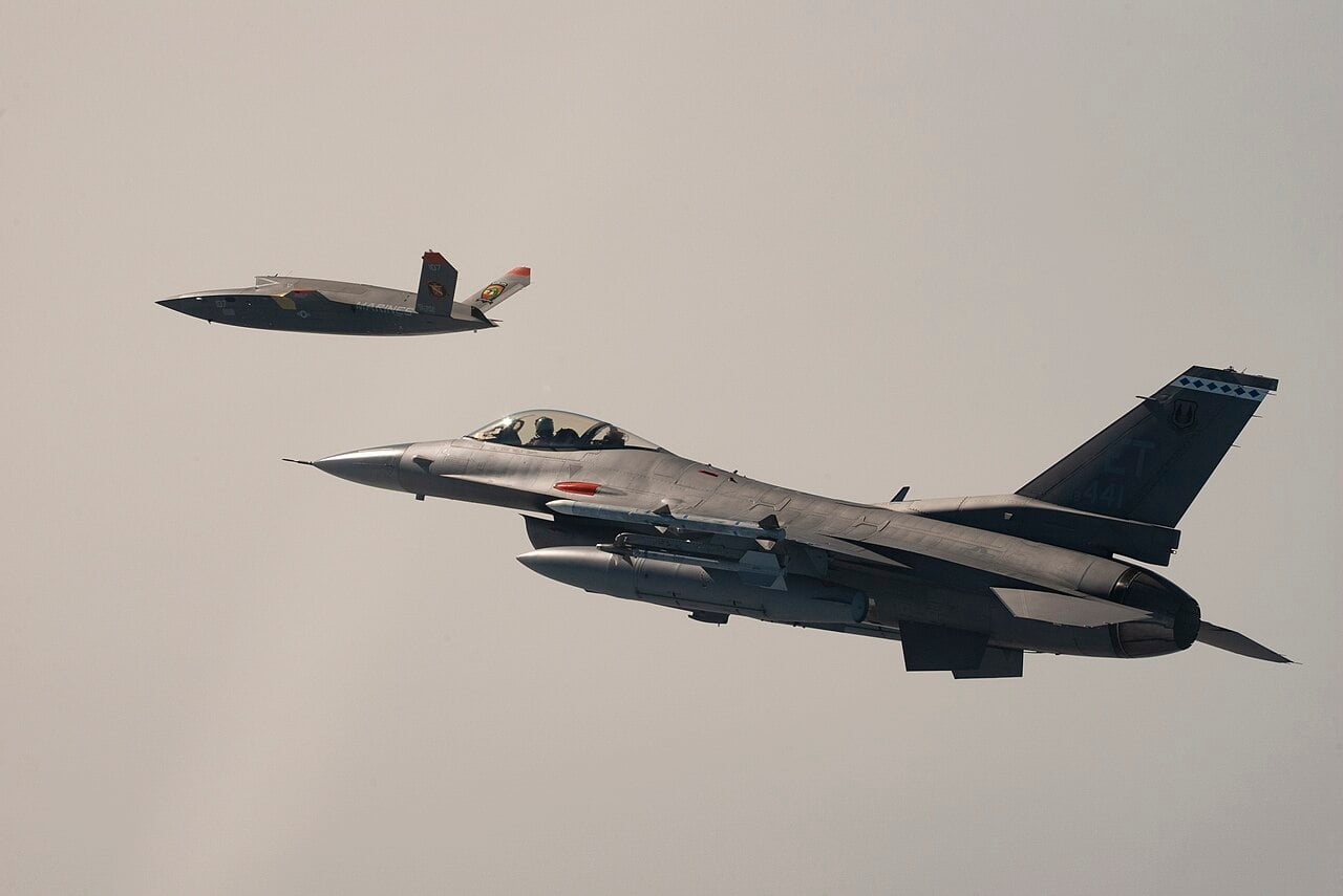 A U.S. Marine Corps XQ-58A Valkyrie flying in formation with a U.S. Air Force F-16 Fighting Falcon