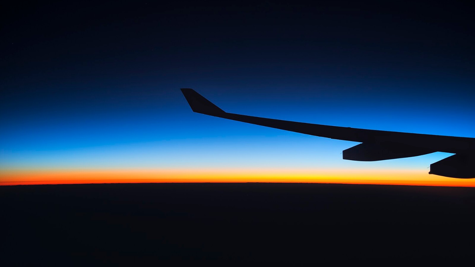 Why Jet Lag Is Worse Flying East, and What Actually Helps Airliner wing silhouetted against a sunrise horizon seen from the cabin window