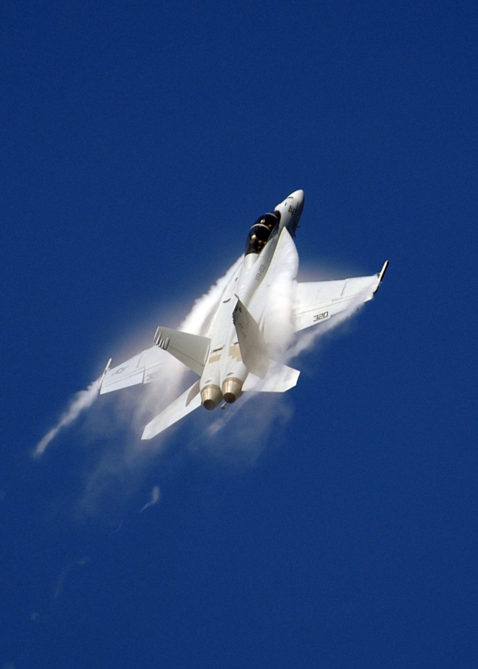 An F/A-18F Super Hornet making a high-speed pass, vapour tearing off the wings.
