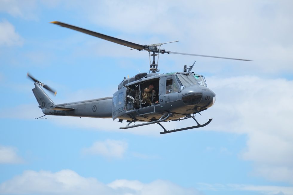 A UH-1H Iroquois in flight with its cabin doors slid wide open the classic Huey silhouette.