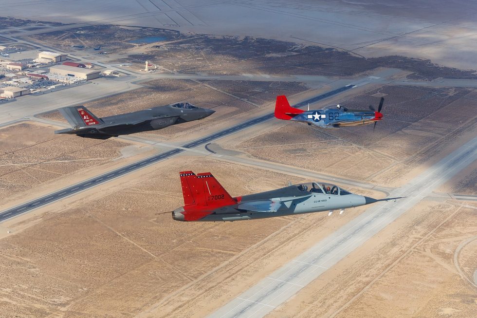 A T-7A Red Hawk flies with an F-35A and a red-tailed P-51D Mustang  past, present and future over Edwards.