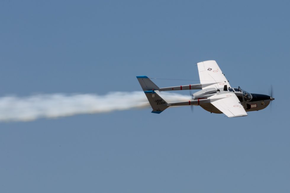 A civilian-owned Cessna O-2 Skymaster warbird banking in flight trailing smoke at an air show