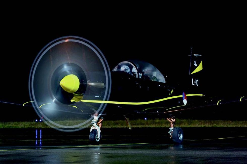 A Royal Netherlands Air Force PC-7 at night, its three-blade propeller arc lit up.
